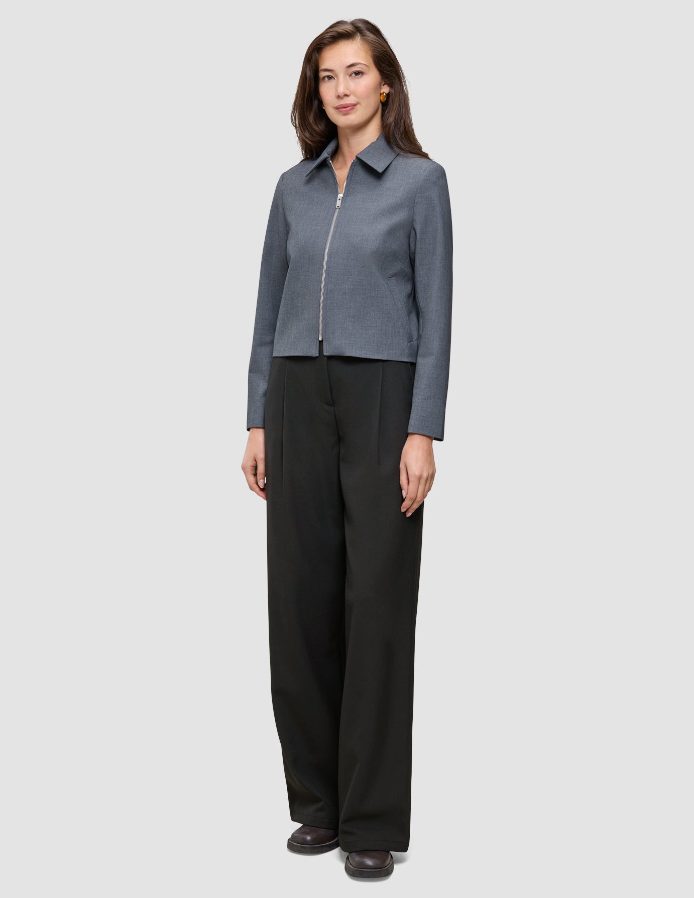 Kvinde iført en Essential Short Zip Jacket i mørkegrå melange og sorte bukser med brede ben.